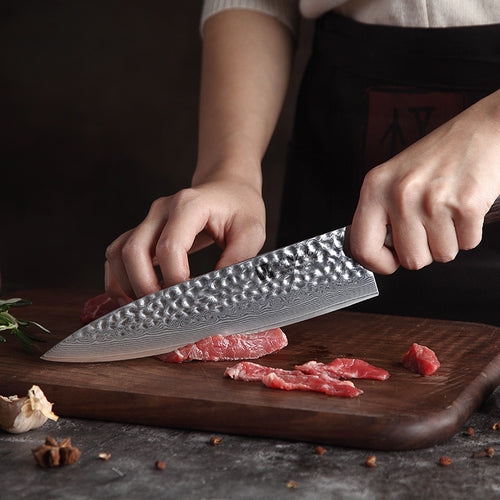 Cuchillo de chef Xinzuo en acero Damasco de 8 pulgadas cortando carne sobre tabla de madera profesional.