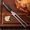 Tenedor trinche profesional Xinzuo de acero inoxidable con mango oscuro sobre tabla de madera con pollo asado.