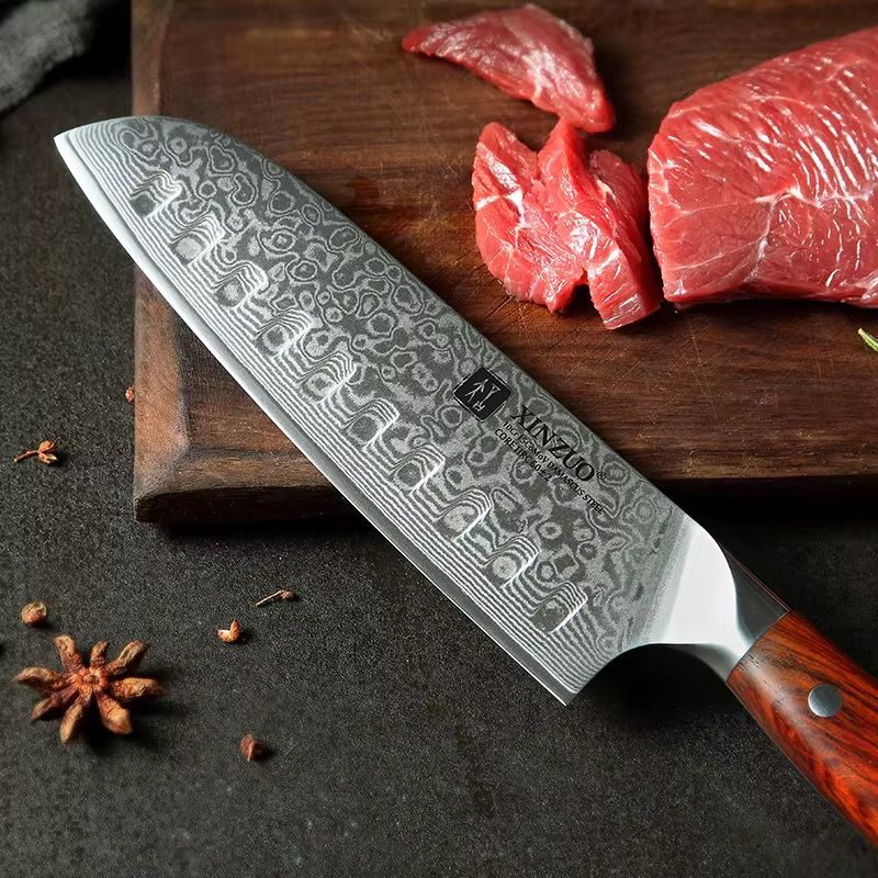 Cuchillo Santoku Xinzuo de acero de Damasco con 67 capas y mango de madera sobre tabla con carne.