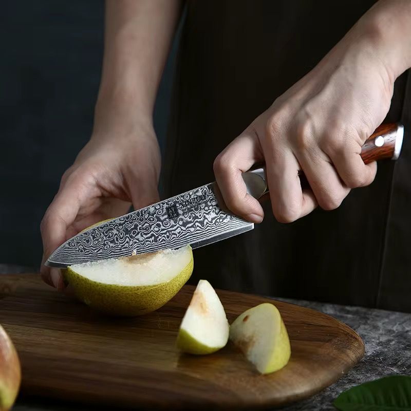 Cuchillo Chef Xinzuo de acero Damasco de 67 capas cortando fruta sobre tabla de madera, mango de Rosewood.