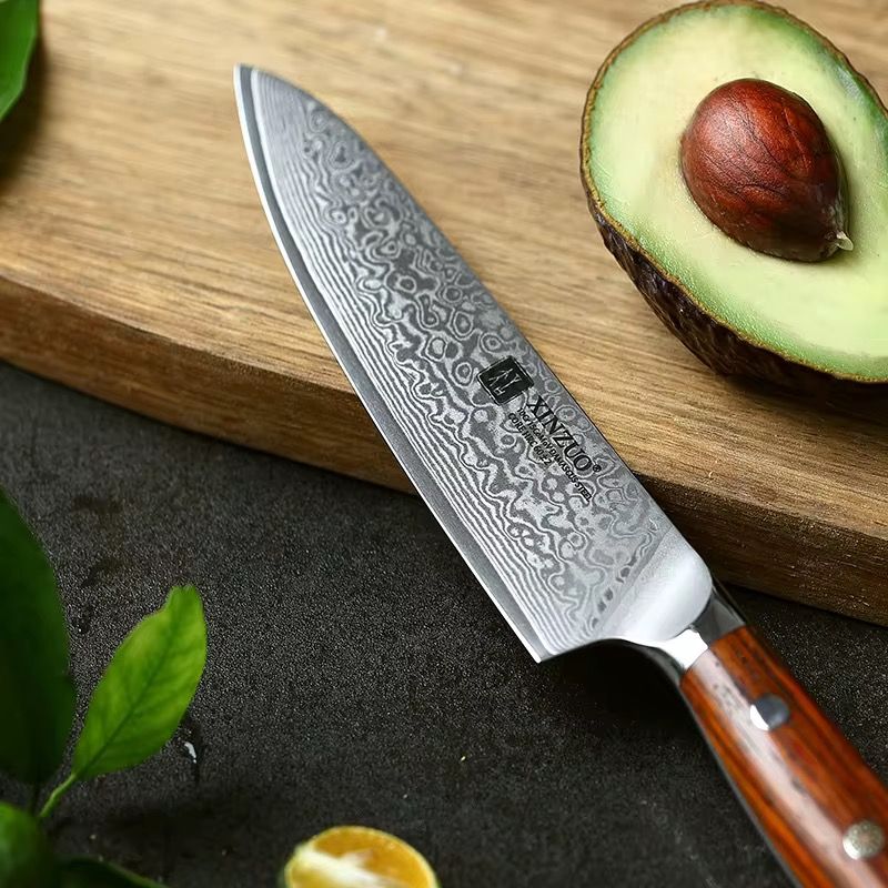Cuchillo de chef Xinzuo de acero Damasco de 67 capas y mango de madera sobre tabla, junto a un aguacate.