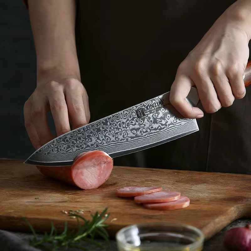 Chef cortando embutido con cuchillo Xinzuo de acero de Damasco profesional sobre tabla de madera.